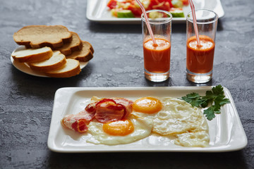 Daily Breakfast. Fried egg with bacon, carrot juice, vegetable salad, bread. On dark stone background