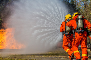 Firefighter using extinguisher and water from hose for fire fighting, Firefighter spraying high pressure water to fire with copy space.