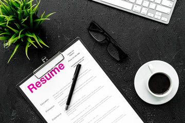 Review resumes of applicants. Resume on black work desk with coffee, glasses, keyboard top view