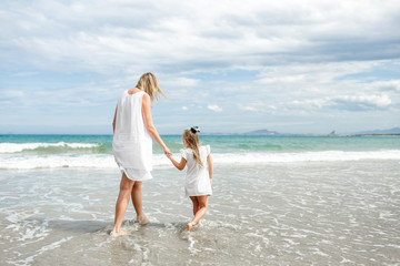 Back view family mother and daughter walking at beach enjoying tropical summer vacation.