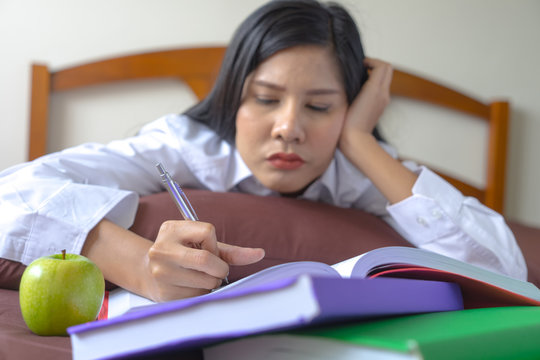Young Asian woman reading books on bed feeling upset. Serious girl feeling bad, nervious about exam.