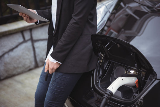 Mid section of woman using digital tablet while charging electric car