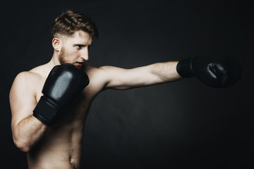 Fototapeta na wymiar Side view portrait of a young man wearing boxing gloves and training in a studio.