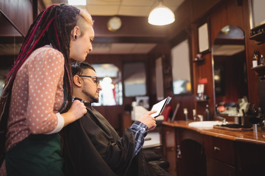 Client showing digital tablet to female barber