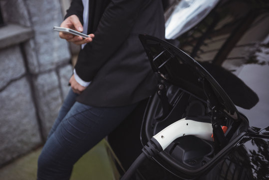 Mid section of woman using mobile phone while charging electric car