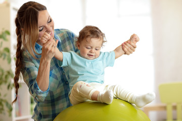 Happy mother and baby toddler on fitness ball in nursery at home. Gimnastics for kids on fitball.