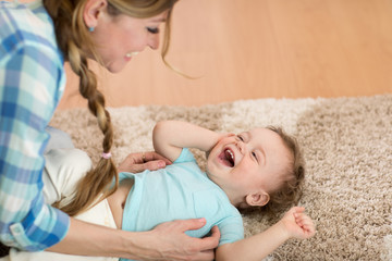 Loving mom tickling her little baby kid on carpet at home