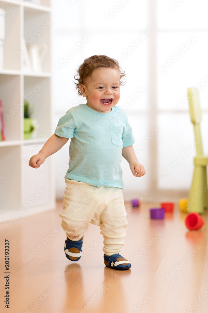 Wall mural First steps of baby toddler learning to walk in living room. Footwear for little children.