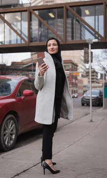 Young woman with smartphone standing on sidewalk