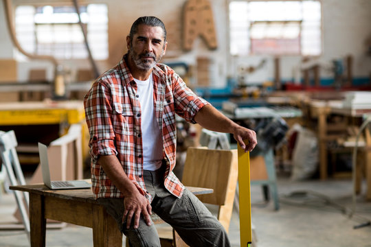 Portrait of mature man sitting on table in workshop