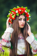 beautiful girl is standing with a wreath of poppies, daisies and leaves on her head in an embroidered shirt