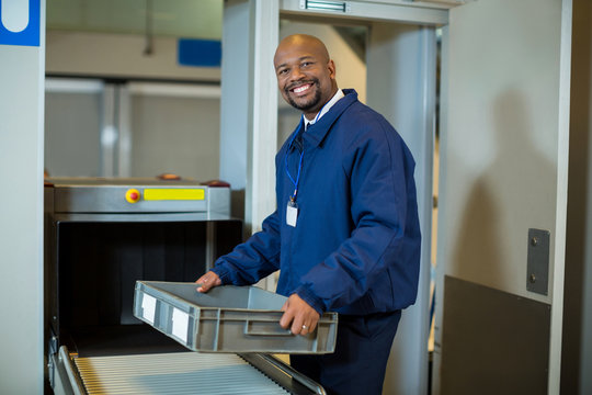 Smiling airport security officer holding a crate near conveyor belt