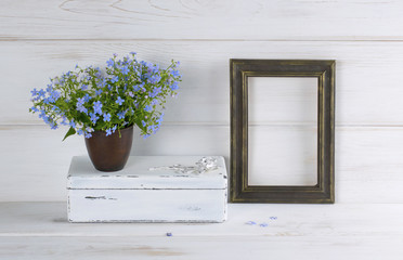 Forget-me-not flowers bouquet in clay cup, vintage casket and photo frame on white wooden shabby board