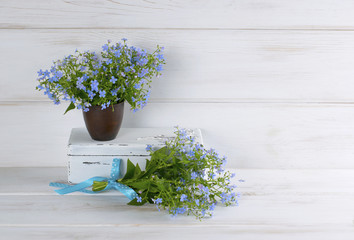 Forget-me-not flowers bouquet in clay cup and vintage casket on white wooden shabby board