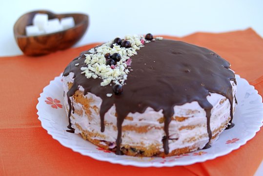 Sponge cake with a cream of cream cheese, covered with chocolate icing. Decorated with grated white chocolate and black currant berries