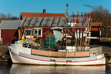 Fototapeta na wymiar Small fishing boat moored in the evening at the docks with forklift and building in background. Names and logos removed. Location Gronhogen on Oland, Sweden.
