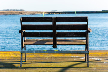 Empty wooden bench at the end of a pier with a blurred view of harbor inlet and coastland. Location Gronhogen on Oland, Sweden.