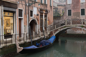 Fototapeta na wymiar A venitian street canal with bridge and boats in Italy