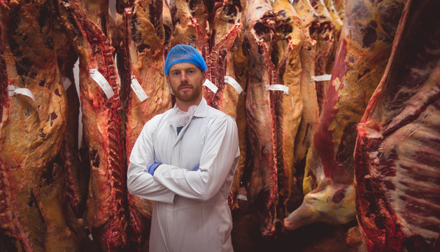 Portrait of butcher standing with arms crossed in meat storage room