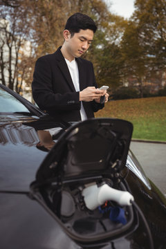 Man using mobile phone while charging electric car