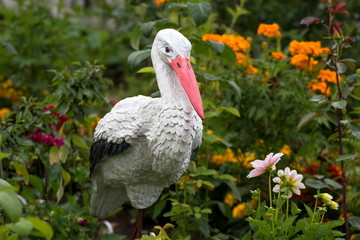 The figure of a stork bird, a garden ornamental decoration stands among the flowers.