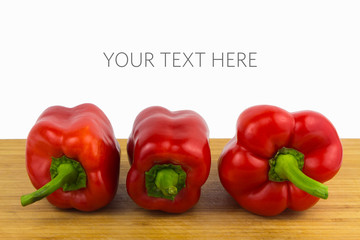 Three red bell peppers in a row on wooden cutting board