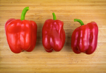 Three red bell peppers on bamboo cutting board