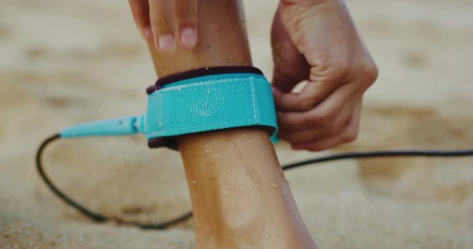 Close up of woman putting on her leash going surfing