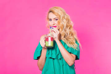 Portrait of smiling young woman drinking smoothie juice on pink background