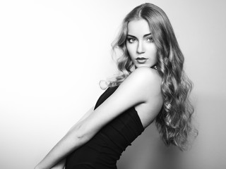 Portrait of beautiful young blonde girl in black dress. Fashion photo. Long Hair