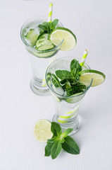Fresh detox spring cocktail with mint, lime, ice, cucumber, straw on soft white wooden background, top view, closeup.