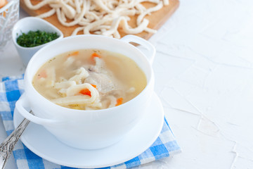 Chicken soup with homemade noodles in a white ceramic soup plate on a white table, horizontal, copy space