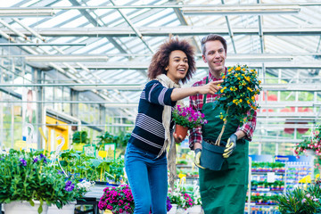 Full length of a handsome and friendly worker helping a female customer with the purchase of an orange decorative houseplant in a modern flower shop 