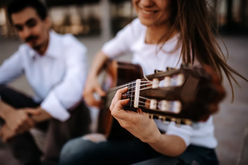 Sitting on the stairs and playing guitar. Girl playing guitar while sitting with her male friend outdoors in the city.