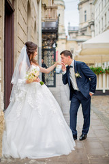 Groom kisses hand of beautiful bride, on background of old street of Lviv, Ukraine