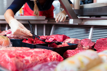 Meat in a butcher shop display being put in by sales woman, close-up