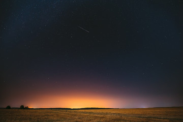 Fototapeta na wymiar Natural Night Starry Sky Above Field Meadow. Glowing Stars, Meteorite