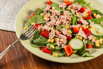 Fresh spinach salad with tuna, cucumber, corn, and red paprika on a plate