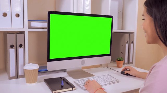 young woman sitting in front of display with green screen. girl using ps mouse playing game or working with happy smile. side view worker sitting at the workspace