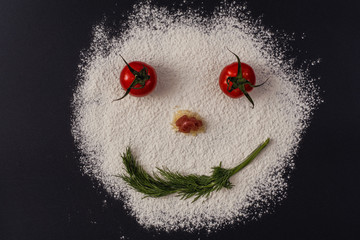 Photo of smiling faces from tomato parsley flour lying on a black