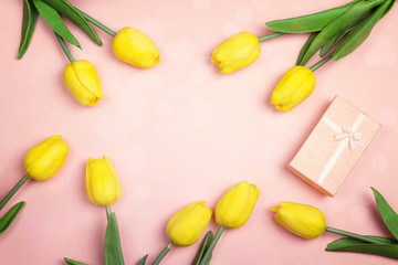 Pink background with yellow tulips and gift box. Flat lay, top view with copy space.