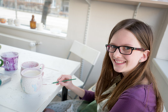 Happy teenage girl painting pottery