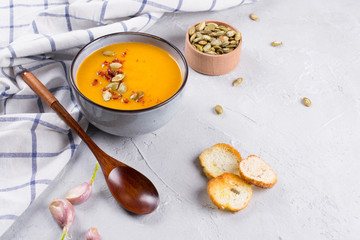 Pumpkin cream soup with seeds, toast and seasoning in a ceramic bowl on a table. Copy space
