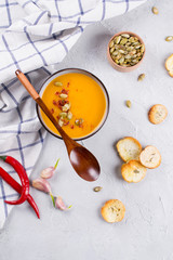 Pumpkin cream soup with seeds, toast and seasoning in a ceramic bowl on a table.