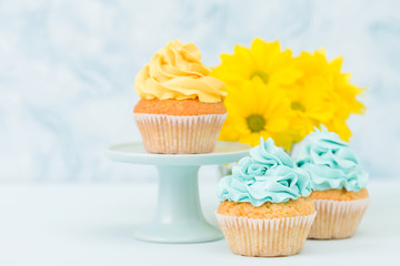 Cupcake with sweet yellow cream decoration and bouquet of yellow chrysanthemum in retro shabby chic vase on blue pastel background.