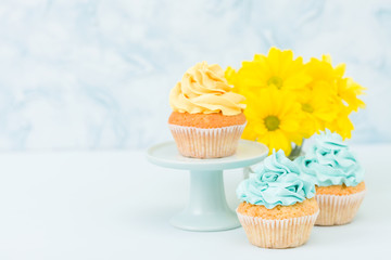 Cupcake with sweet yellow cream decoration and bouquet of yellow chrysanthemum in retro shabby chic vase on blue pastel background.