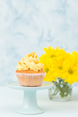 Cupcake with yellow cream decoration on vintage stand and bouquet of yellow chrysanthemum in glasses vase.