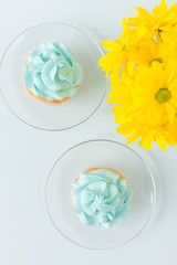 Cupcake with sweet blue cream decoration on sauser and bouquet of yellow chrysanthemum in glasses cup. Flat-lay concept