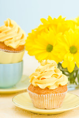 Cupcake with yellow cream decoration and bouquet of yellow chrysanthemum in small glass.