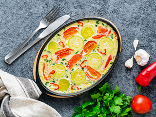 Pan with traditional Italian Frittata on dark gray stone table, forks, parsley, pepper, tomatoes. Scrambled eggs  with a mix of colorful vegetables. Hot omelette. Top view.